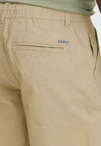 Shorts beiges en tissu léger, dotés d'une taille élastique et d'une poche arrière avec une étiquette "BLEND". Texture lisse, design décontracté.