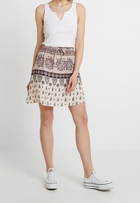 Valkoinen ribattukangas toppi yhdistettynä kuvioituun beige-hameeseen, jossa on kukkakuosi ja nyörivyötärö, täydentää valkoiset lenkkarit.