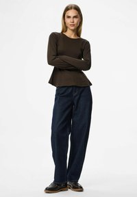 Brun långärmad topp med peplumslut, kombinerad med löst sittande mörkblå denimbyxor och svarta skor med bruna sulor.