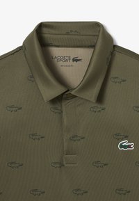 Polo de Lacoste Sport en verde olivo con ajuste regular, que presenta un sutil estampado de cocodrilos en toda la prenda y un logotipo de marca en contraste.