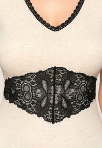 Czarny koronkowy pasek w talii z misternymi wzorami kwiatowymi i liściastymi, z falbanką i wyraźną konstrukcją, na tle beżowej bluzki.