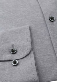 Grijze knoopsluiting shirt detail, met een zachte stofstructuur, twee zwarte knopen op de manchet en een keurig genaaide zakflap.