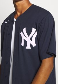 Merensinisen lyhythihainen baseball-paita, jossa edessä napit ja suuri valkoinen NY-logo vasemmalla rinnalla. Hengittävä kangas.