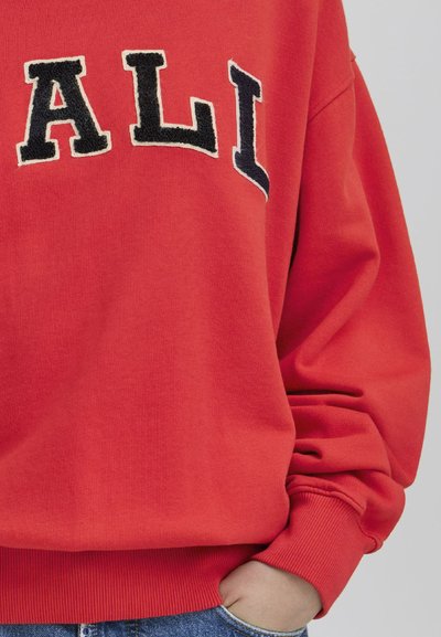 Rød hettegenser med store, svarte bokstaver som skriver "ALL." Har ribbede mansjetter og kant, myk tekstur og en avslappet passform.