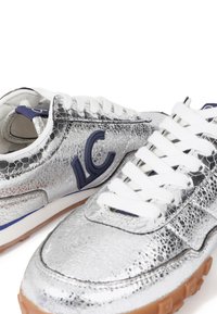 Zapatillas plateadas con acabado texturizado, cordones blancos y un logotipo azul. Presenta una suela de goma y una franja azul en contraste en el costado.