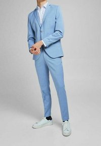 Ljusblå kostym med slim fit, enkel knappstängning och vit mönstrad skjorta under; bärs med vita sneakers. Slät textur.