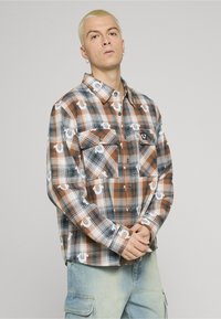 Camicie di flanella a quadri in arancione, nero e bianco, con due tasche sul petto, chiusure con bottoni e un motivo a logo ripetuto.