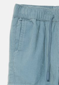 Lyseblå corduroy-shorts med elastisk midjebånd, snor og sidelommer. Stoffet har en vertikal ribbestruktur.