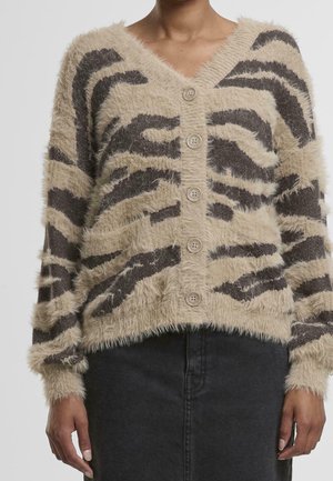 Femme portant un cardigan beige et marron à rayures duveteuses boutonné avec des manches longues et une jupe noire.
