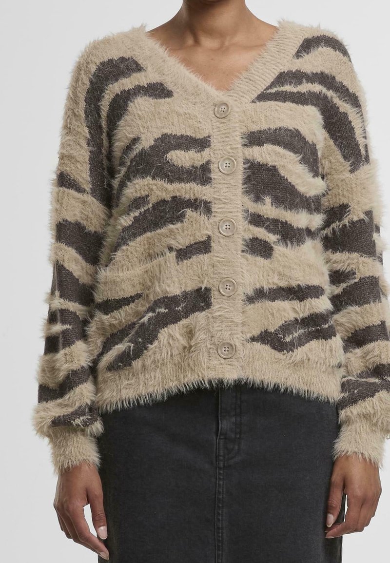 Femme portant un cardigan beige et marron à rayures duveteuses boutonné avec des manches longues et une jupe noire.
