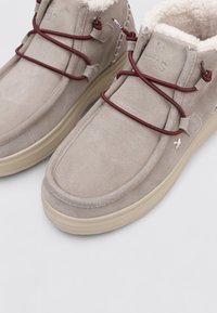 Botas de tobillo de ante beige con forro de pelo sintético, con cordones elásticos burdeos, punta redondeada y suela de goma texturizada.