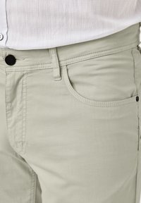 Hellgrüne Hose mit glatter Textur, ausgestattet mit einer vorderen Tasche, Gürtelschlaufen und einem schwarzen Knopfverschluss.