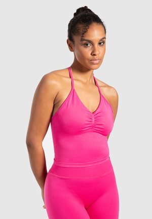 Enganliegendes pinkes Haltertop mit gerafftem Detail an der Vorderseite, aus einem dehnbaren Stoff gefertigt. Kombiniert mit passenden, hoch taillierten Leggings.
