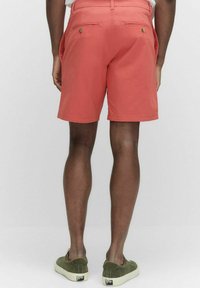 Korallshorts med en slät yta, elastisk midja och två bakfickor. Bärs med gröna slip-on skor.