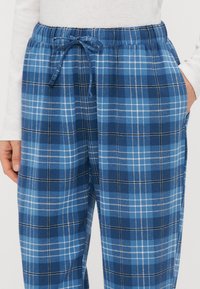 Μπλε καρό παντελόνι από μαλακό ύφασμα, με ελαστική μέση και κορδόνι για ρύθμιση, πλαϊνές τσέπες και μείγμα ανοιχτόχρωμων και σκούρων μπλε τετραγώνων.