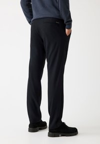Mustad püksid, mis on valmistatud siledast, kergest kangast ja millel on slim fit lõige. Omab külgtaskuid ja tagumist welt-taskut. Kandmine mustade kingadega.