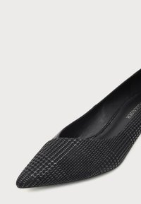 Chaussure plate noire à bout pointu avec motif texturé brillant effet peau de serpent et doublure intérieure en cuir lisse.
