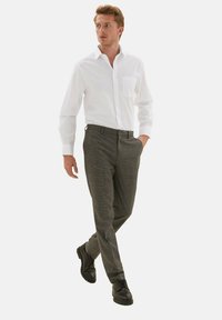 Camisa blanca de manga larga con un bolsillo, combinada con pantalones de cuadros grises y zapatos de cordones negros. El conjunto tiene un corte entallado y texturas sutiles.