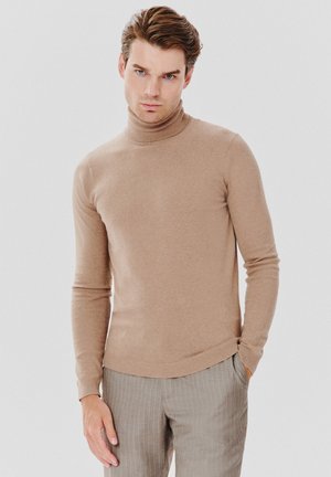 Jasnobrązowy sweter typu golf w miękkim dzianinowym materiale, z długimi rękawami i dopasowanym krojem, w zestawie z szarymi spodniami w prążki.