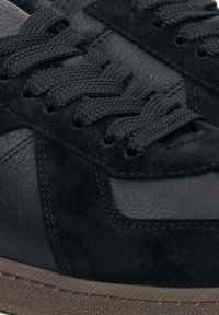 Černé tenisky kombinující hladkou kůži a strukturovanou suede. Vybavené černými tkaničkami a hnědou gumovou podrážkou.