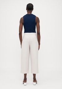 Marineblauw mouwloos topje met een kraag, gecombineerd met hoge taille, brede lichtbeige broeken. Eenvoudig ontwerp en gladde textuur.