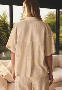 Beige texturerad skjorta med avslappnad passform, korta ärmar och ett subtilt randmönster, med en klassisk krage och en slät finish.