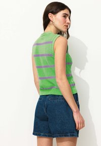 Top vert sans manches avec des rayures violettes, en tissu tricoté texturé, associé à un short en jean bleu foncé. Design visible au dos.