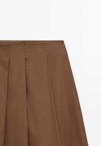 Hnědá skládac�í sukně vyrobená z lehkého materiálu, s bočním zipem a čistým designem pasu. Hladká textura, dobře padnoucí střih.