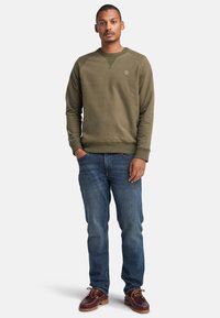 Sudadera verde oliva con cuello redondo y puños acanalados, combinada con jeans de mezclilla azul de pierna recta y zapatos de barco marrones.