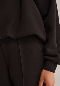 Felpa nera e pantaloni in un morbido tessuto testurizzato. La felpa ha una vestibilità ampia con polsini arricciati, mentre i pantaloni presentano una silhouette elegante e sartoriale.