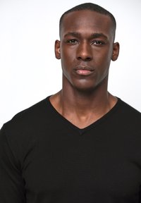 Svart v-ringad tröja med en åtsittande design och en mjuk textur, bärs av en person med kort hår och ett neutralt uttryck.