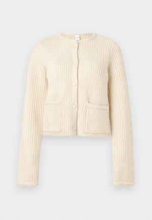 Cardigan recortado color crema, con tela texturizada y acanalada verticalmente, cierre delantero con botones y dos bolsillos de parche.