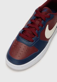 Tenis Nike com parte superior em couro bordeaux e azul-marinho, com perfurações na caixa dos dedos, atacadores azuis-marinho e logótipo swoosh em off-white.