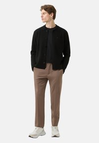 Černý kardigan na zapínání přes knoflíky přes námořnicky modrou košili, doplněný světle hnědými kalhotami a bílými teniskami. Kardigan má nášivku s kapsou.