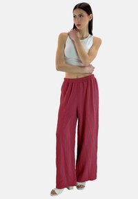 Pantalones anchos de pierna ancha texturizados en rojo con cinturilla elástica, combinados con una camiseta blanca sin mangas ajustada y sandalias blancas de tacón grueso.