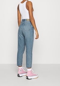 Světle modré džíny s vysokým pasem a rovnými nohavicemi, s zadními kapsami, doplněné růžovými teniskami s vysokým svrškem.