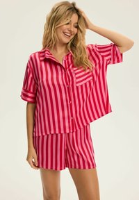 Satynowy zestaw do spania w jasnoróżowym kolorze w białe pionowe paski; krótki rękaw, z kołnierzykiem, z kieszenią na piersi oraz pasujące szorty.