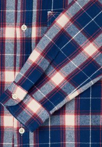 Camicia in flanella a quadri blu, rossa e bianca, caratterizzata da un polso con bottoni, una texture liscia e un design a pattern con quadretti di diverse dimensioni.