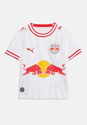 Λευκή φανέλα ποδοσφαίρου Red Bull Salzburg με κόκκινη επένδυση, λογότυπα Puma και δύο κόκκινους ταύρους να κοιτούν έναν κίτρινο κύκλο μπροστά.