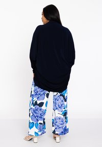 Marineblauwe top met lange mouwen, gecombineerd met wijde broekspijpen met een blauw bloemenpatroon op een witte achtergrond. Vierkante blokhakken.