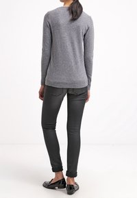 Grå stickad tröja med lång ärm, rund halsringning och ribbad nederkant, matchad med tajta svarta jeans och svarta slip-on-skor.