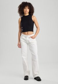 Black ribbed crop top with a high neckline, paired with loose-fitting white jeans and black platform shoes. Plain background.
