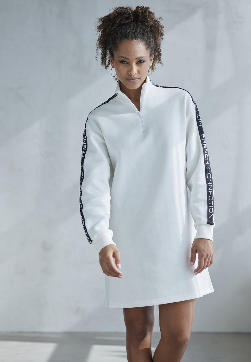 Weißes Sweatshirtkleid mit einem halben Reißverschlusskragen, langen Ärmeln und dunkelblauen Brandingstreifen an den Armen. Weicher Stoff mit einer entspannten Passform.