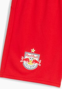 Röda sportshorts i stark röd tyg med Red Bull Salzburg-logotypen, som har ett runt emblem och två röda tjurar. Lätta och andningsbara.