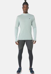 Light blue long-sleeve athletic top paired with dark leggings featuring black and gray paneling. Textured fabric; modern fit design.