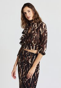 Completo composto da top corto e gonna in tessuto trasparente con stampa leopardata marrone e beige, caratterizzato da dettagli arricciati, maniche lunghe e scollo a goccia.