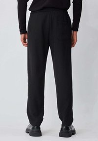Pantalon noir fuselé en tissu lisse, doté d'une ceinture élastique et d'une seule poche arrière, avec des jambes droites et un design minimaliste.