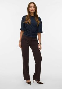 Marineblå kortærmet top med rynkedetalje, kombineret med brune skræddersyede bukser og mørkebrune hælede sko. Glat tekstur hele vejen igennem.