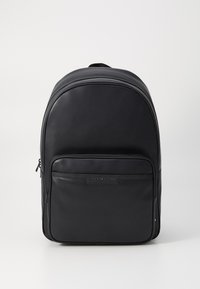 Must värvusega Tommy Hilfiger seljakott, millel on suur peamine sektsioon ja eesmine lukuga tasku, valgel taustal.