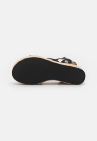 Wedge schoen met zwarte textuurzool, natuurlijke geweven plateau en zwarte banden met een patroon van witte en gele madeliefjes.